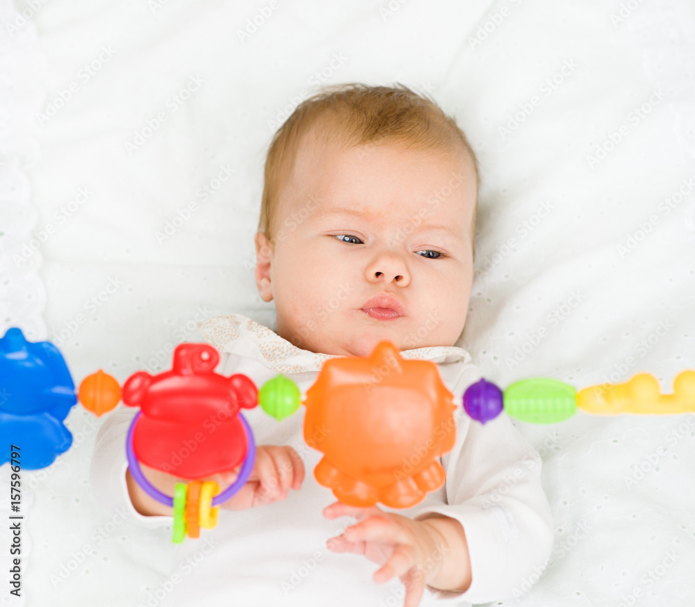 Newborn baby girl playing with toy rattle lying on back Newborn baby girl playing with toy rattle lying on back