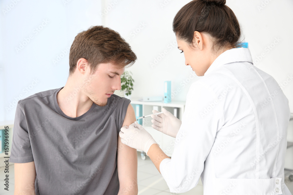Young man receiving injection from medical assistant in clinic Young man receiving injection from medical assistant in clinic