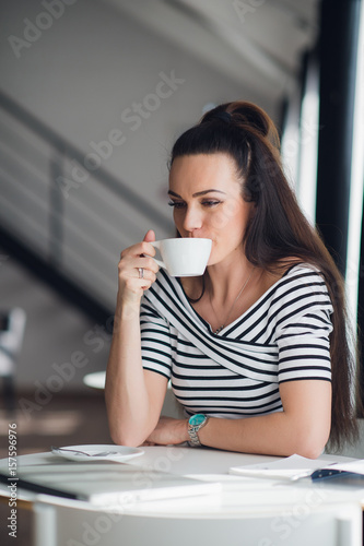 Beautiful young woman holding a cup of coffee looking away and smiling. Cheerful female enjoying a cup of coffee at cafe.