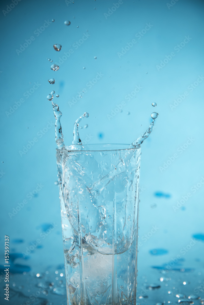 Ice dropped in a glass of water, falling in, making a splash and water droplets