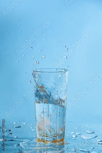 Ice dropped in a glass of water, falling in, making a splash and water droplets
