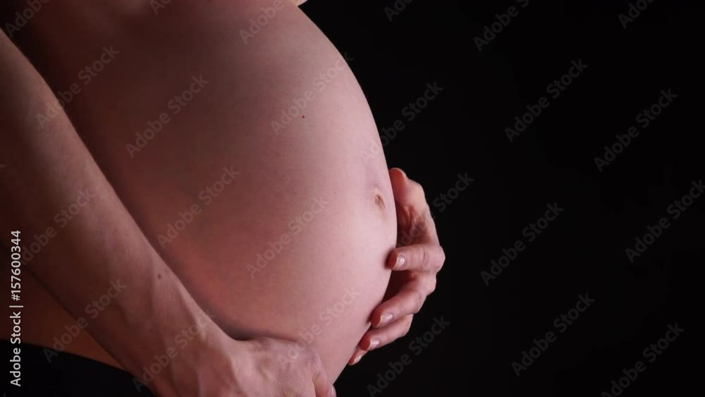 Pregnant woman no face touching caressing her naked big belly, closeup on black. Pregnancy, motherhood, baby anticipation and new life concept. 4K ProRes HQ codec