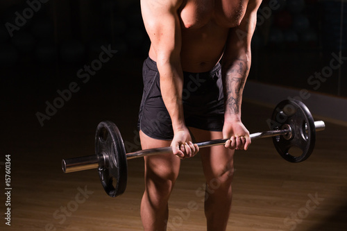 Muscular man working out in gym doing exercises with barbell close-up, strong male naked torso abs.