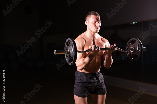 Sporty man doing exercises with barbell on dark background