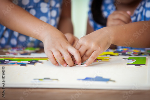 Two children hands helping and trying to connect jigsaw puzzle piece to learn to find solution