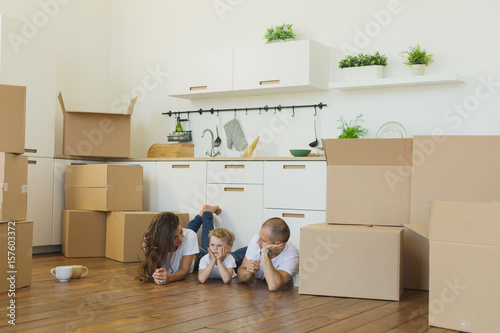 Family lying on floor by open boxes in new home smiling