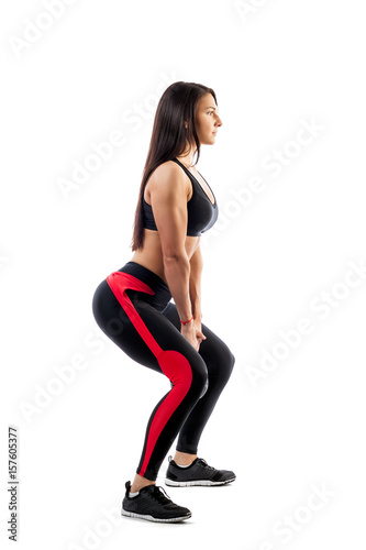 Young woman in sports clothes makes deadlift with weights in semi-sitting position on white isolated background. Side view