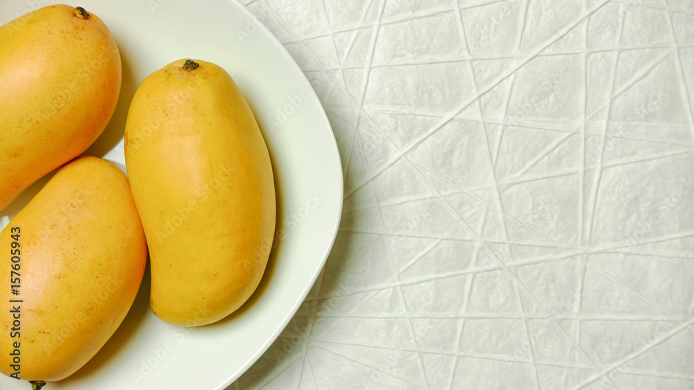 Mangoes in white bowl on white textured paper 