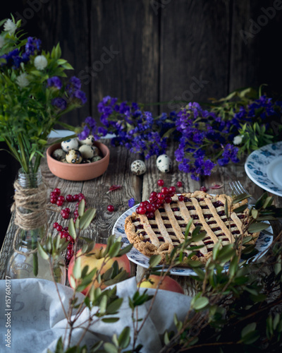 pie with berry filling on a white and blue plate with purple flowers, red currant, green leavesm quail eggsm fresh apples on a wooden table photo