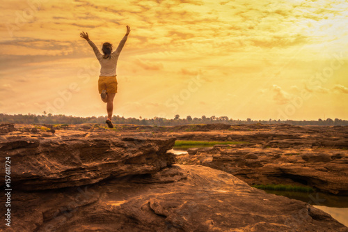 Young woman jumping hands up relaxing in sunset sky landscape outdoor