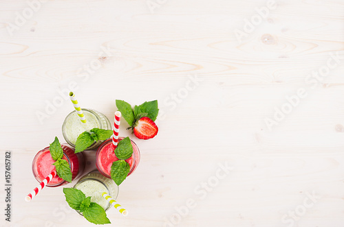 Freshly blended green and red fruit smoothie in glass jars with straw, mint leafs, top view. White wooden board background, copy space.