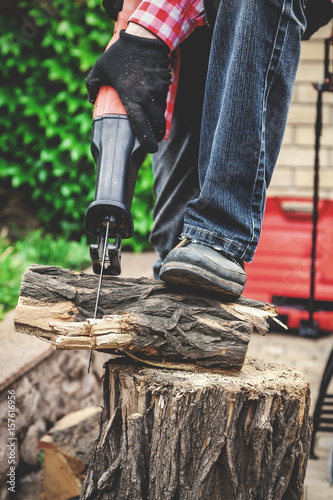 man in plaid shirt sawing piece of wood on stump © glebchik