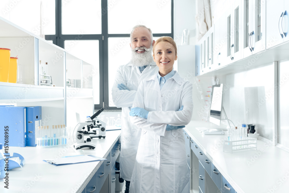 two happy chemists in white coats standing in chemical laboratory with microscopes and flasks two happy chemists in white coats standing in chemical laboratory with microscopes and flasks