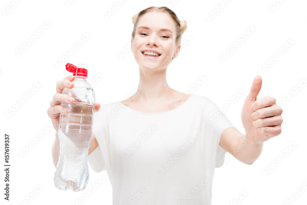 Smiling girl holding bottle with water and showing thumb up isolated on white
