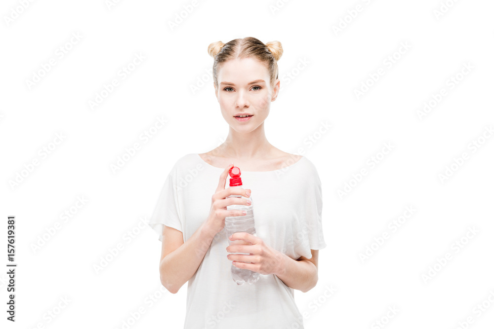 Attractive young woman in white t-shirt holding bottle with water and looking at camera Attractive young woman in white t-shirt holding bottle with water and looking at camera