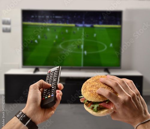 Viendo el partido de futbol en la televisión mientras como hamburguesa. photo