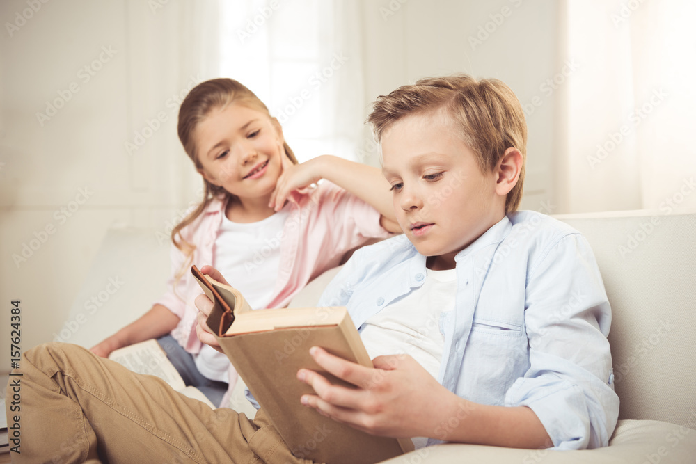 smiling caucasian sister and brother reading book together at home smiling caucasian sister and brother reading book together at home