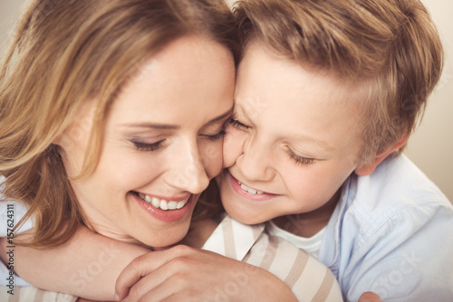 Close-up portrait of happy mother and cute little son hugging together at home