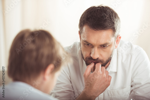 portrait of pensive bearded man with hand on chin looking away with son near by