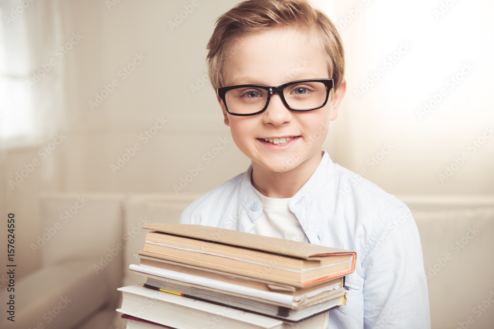 Adorable little boy in eyeglasses holding pile of books and smiling at camera Adorable little boy in eyeglasses holding pile of books and smiling at camera