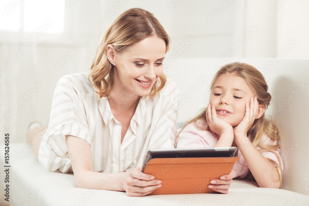 smiling mother and daughter using digital tablet while lying on sofa at home smiling mother and daughter using digital tablet while lying on sofa at home