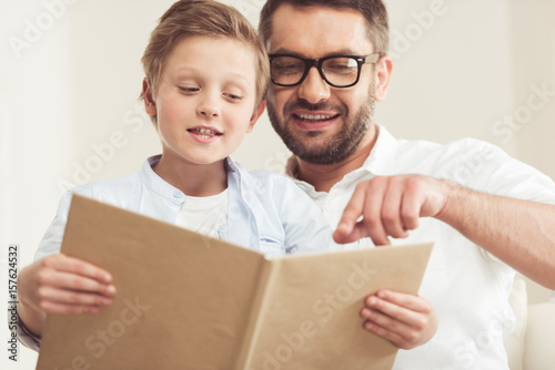 little son with father reading book at home together