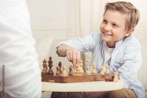 portrait of smiling boy looking at father during chess game at home