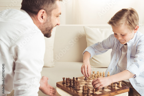 side view of happy little boy playing chess together with father at home