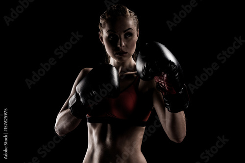 caucasian muscular sportswoman exercising in boxing gloves isolated on black
