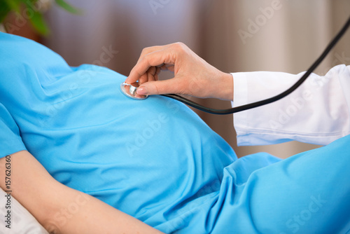 Cropped shot of doctor with stethoscope listening belly of pregnant woman lying on hospital bed