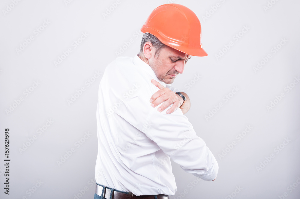 Side view of architect wearing hardhat holding shoulder like hurting Side view of architect wearing hardhat holding shoulder like hurting