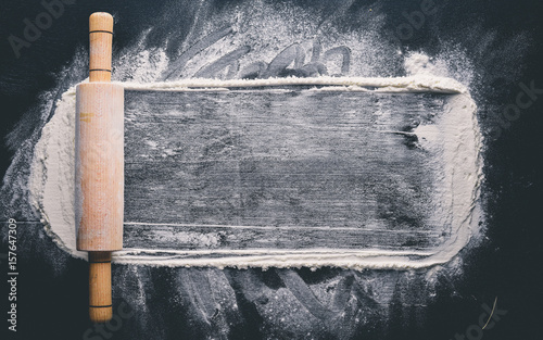 Rolling pin and white flour on a dark background. Free space for text . Top view.