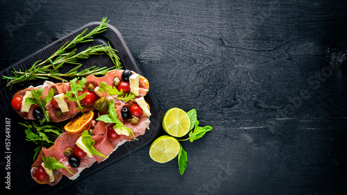 Bruschetta with meat, olives, herbs and parmesan cheese on bread. Cold snacks. Italian cuisine. On Wooden background.