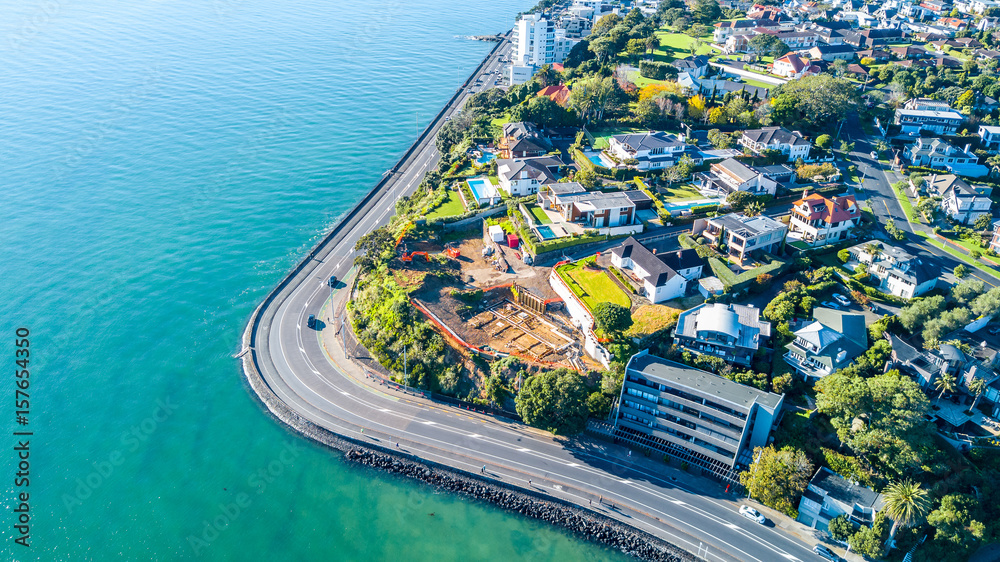 Aerial view on a road running along sea shore with residential suburbs on the background. Auckland, New Zealand.
