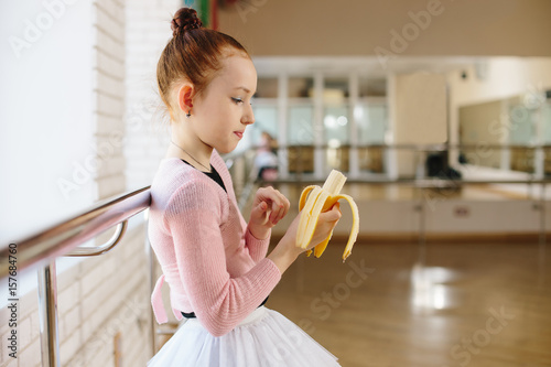 Girl ballerina eating a banana in ballet class