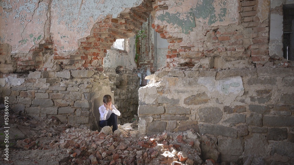 The boy hides and cries, in a ruined building after the war, lost, fear, loneliness, threat, loss