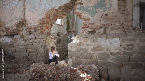 The boy hides and cries, in a ruined building after the war, lost, fear, loneliness, threat, loss photo