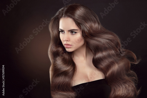 Healthy hair. Wavy hairstyle. Beautiful brunette woman model with clean skin advertising shiny brown straight long hair isolated on brown dark background.