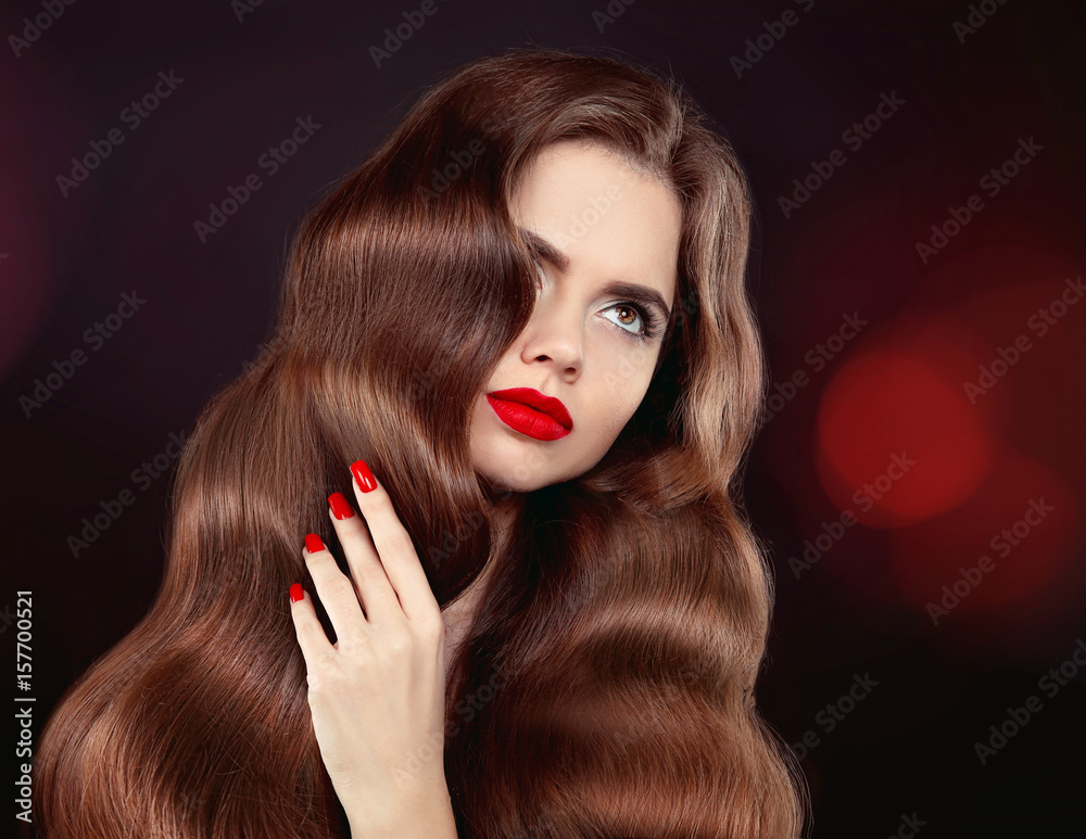 Fototapeta premium Healthy hair. Red lips & manicure. Wavy hair. Beautiful model girl portrait with shiny brown straight long hairstyle and makeup isolated on black background. Elegant woman.