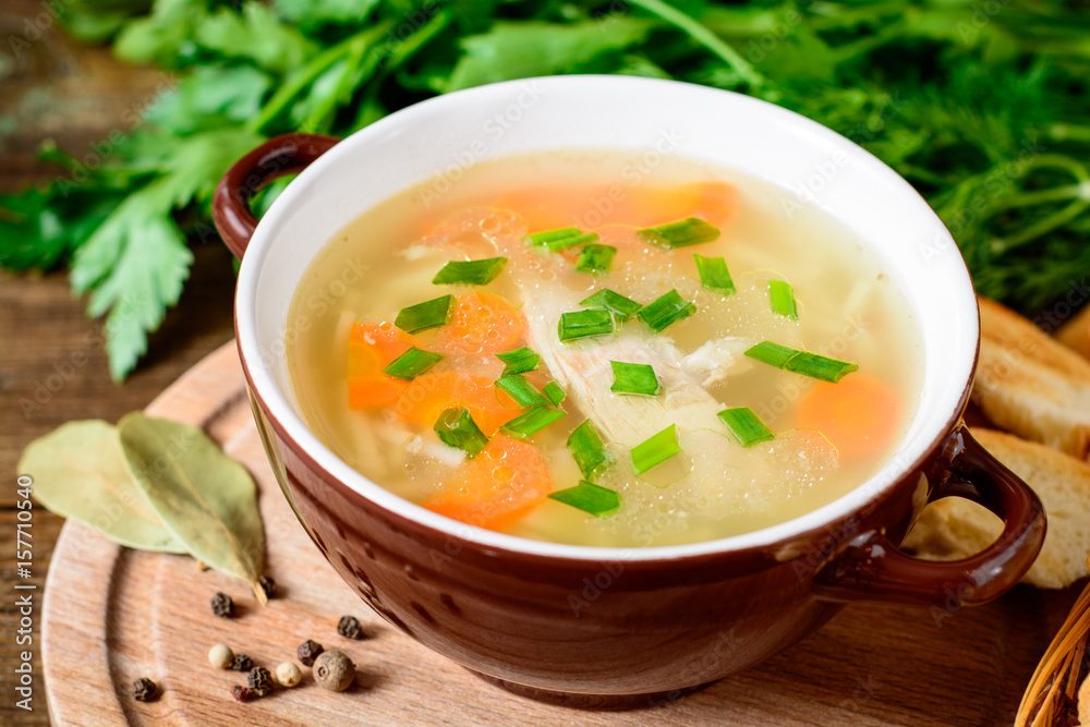 Homemade chicken soup with noodles and vegetables in ceramic bowl on wooden table.