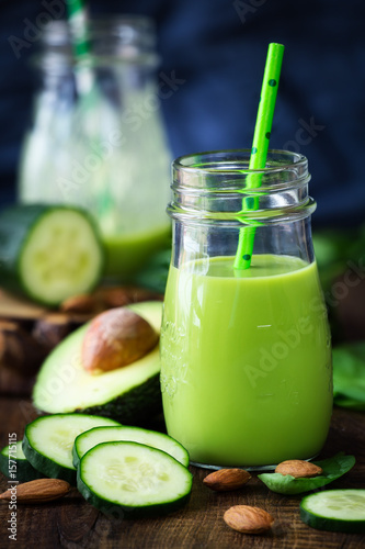 Healthy food concept - green detox smoothie with avocado, cucumber, spinach and almonds in glass jar with a straw