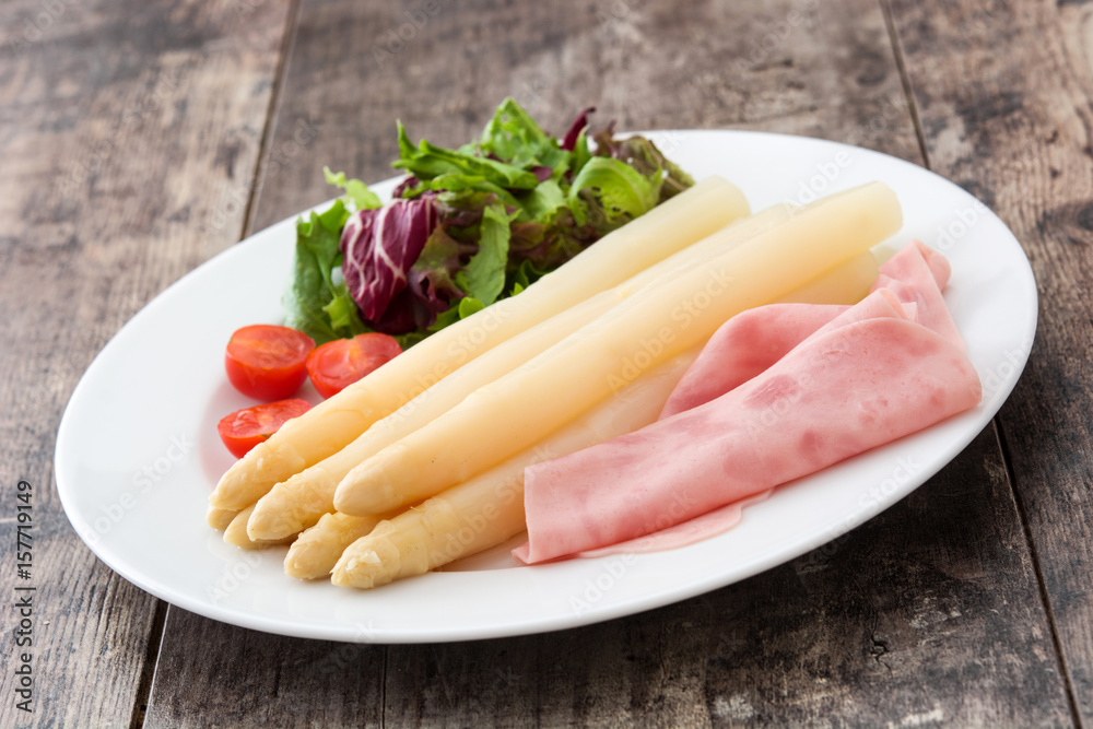 White asparagus with salad and ham on wooden background
