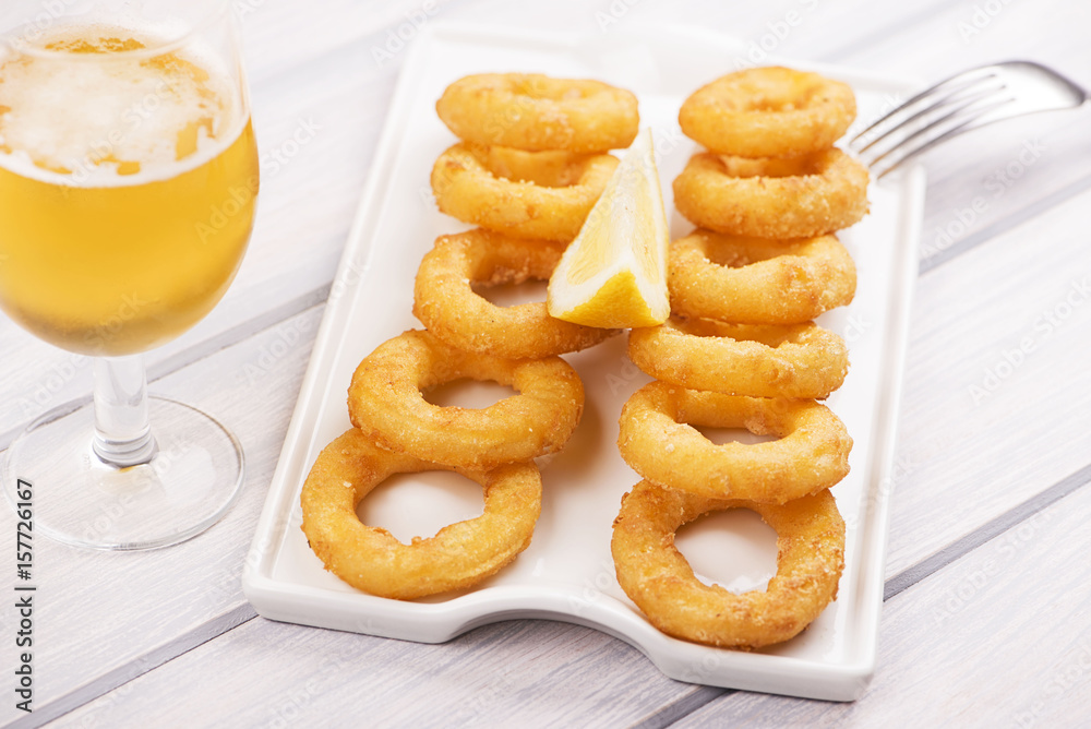 Plate of squid a la romana next to a beer on white wooden table. Food squids. Horizontal shoot. Plate of squid a la romana next to a beer on white wooden table. Food squids. Horizontal shoot.