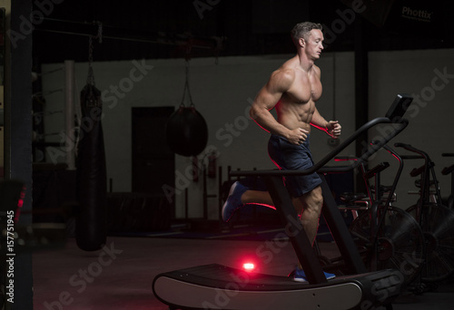 Платно Muscular White Caucasian man running on treadmill machine in a dark grungy gym w