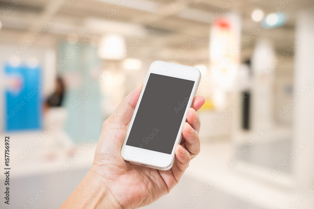 Hand holding empty screen mobile phone with abstract blurred interior background