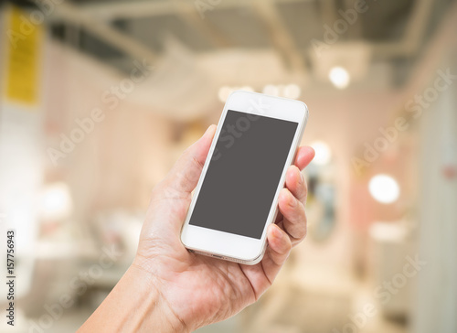 Hand holding empty screen mobile phone with abstract blurred interior background