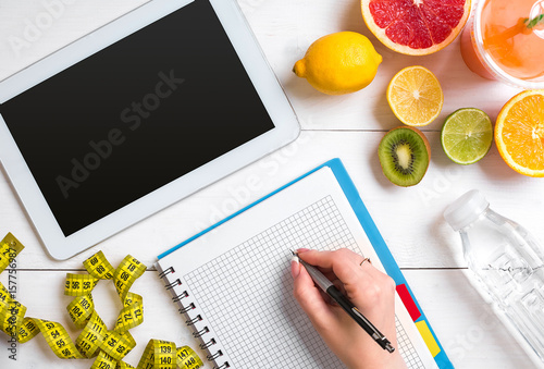 Fresh juice in glass from citrus fruits - lemon, grapefruit, orange, notebook with pencil on white wooden background
