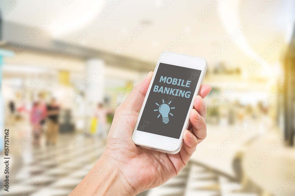 Hands holding mobile phone with Mobile banking word on screen. blurred image of shopping mall background