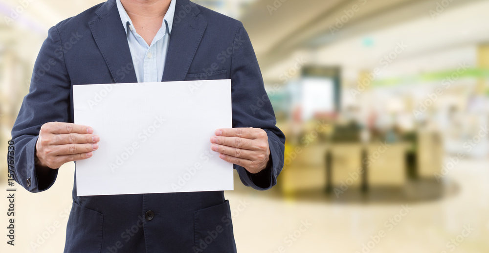 Man holding blank white board on blur shopping mall background Man holding blank white board on blur shopping mall background