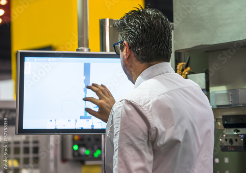 Worker entering data in CNC machine at factory floor to get the production going